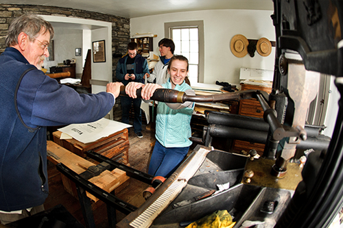 Liz Morris '16 presses an inked plate onto paper in the print shop at the Farmer's Museum with the help of Ted Shuart.