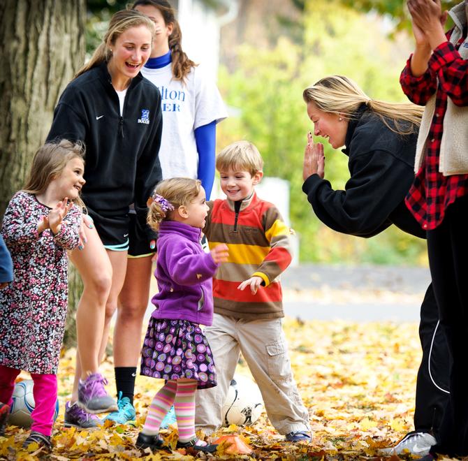 Members of Hamilton's Women's Soccer team and Victoria Freeman '16, right, cheer on three-year-old Clara Shaw as they play relay games at Fall Fest.