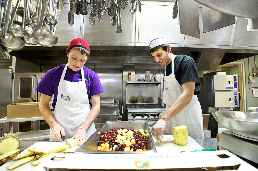 Kurt Eyerer '15, left, and Andrew Dubowitz '13 cut up fruit for dinner service as they volunteer at the Rescue Mission of Utica as part of Hamilton Serves