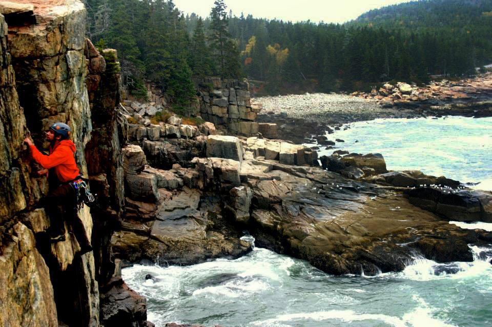 John Pikus '16 scales a cliff above the crashing ocean in Acadia National Park.