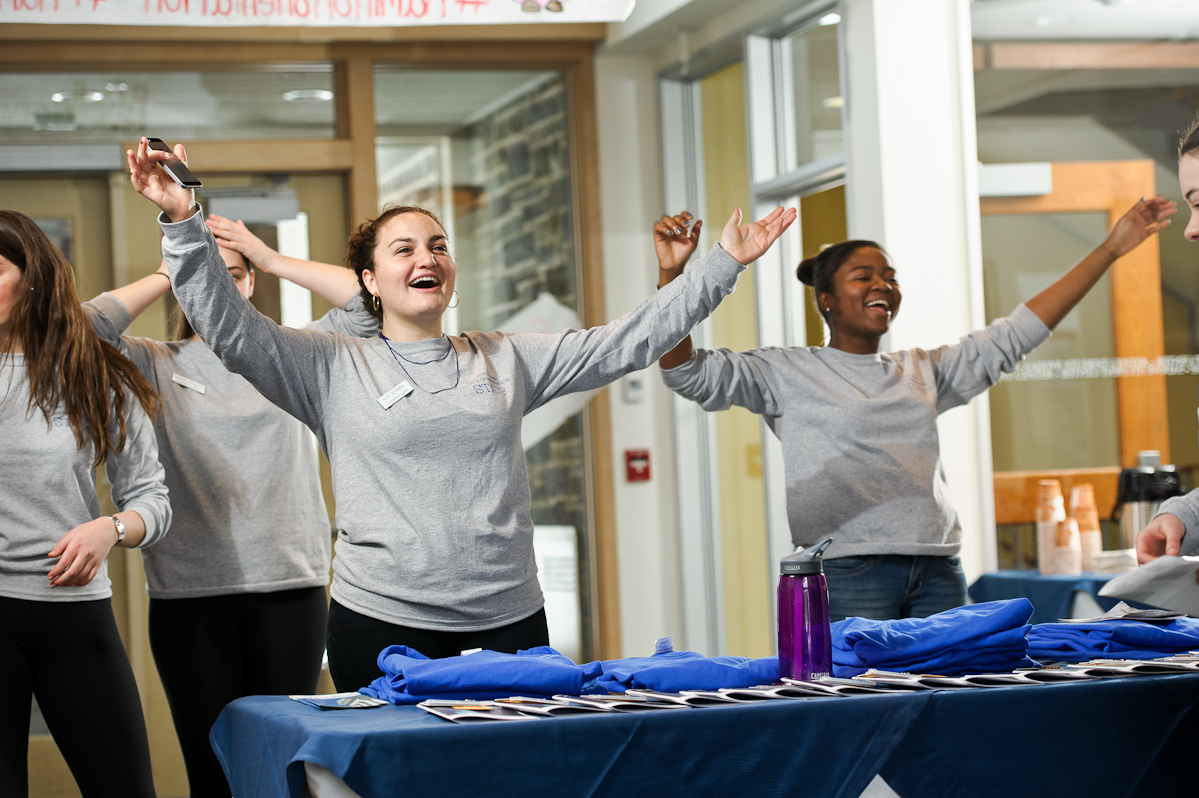 Orientation leaders Allie Goodman '15, left and Geleece Brady '16, right, raise their arms to welcome January first-year admits to campus in the lobby of Sadove Center